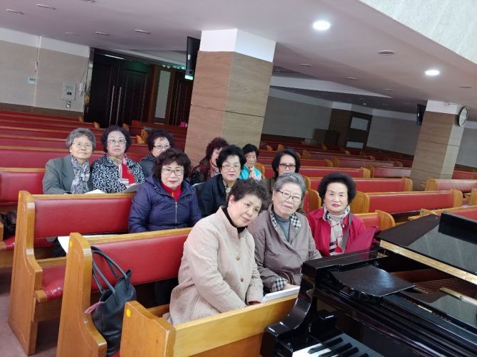 붉은 긴 의자에 앉은 여러 사람이 그랜드 피아노 옆에서 함께 사진을 찍는 모습