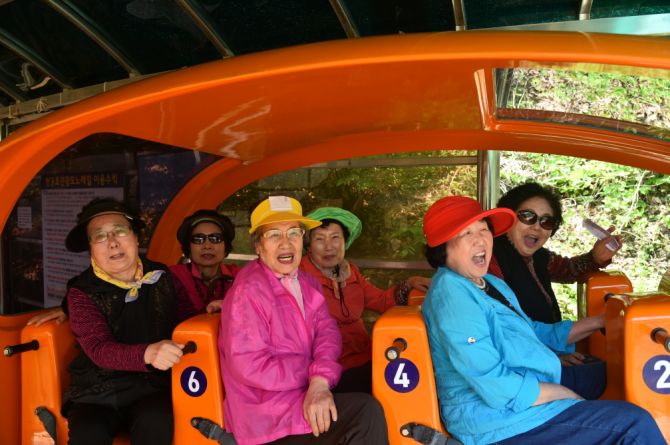 야외 나들이 장소에서 주황색 관람 차량에 나란히 앉아 웃는 사람들